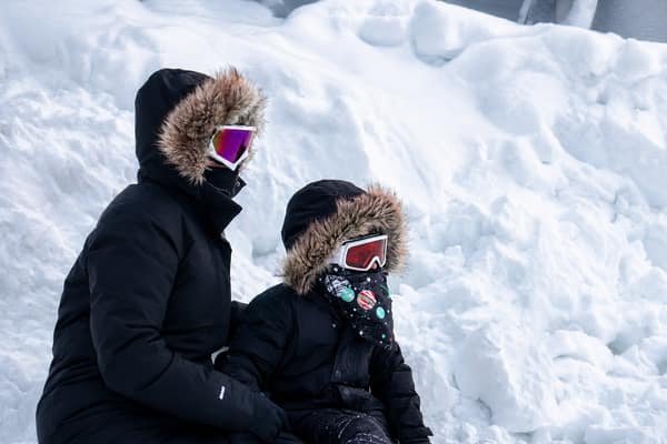 Two people in fur-hooded parkas beside a deep snowbank in Kaktovik