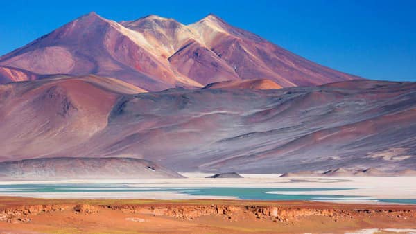 Colorful mineral mountains above a turquoise altiplano lagoon