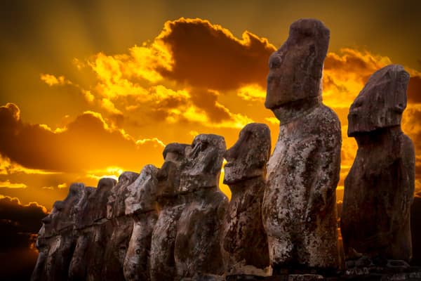 Standing moai beneath orange clouds at sunset