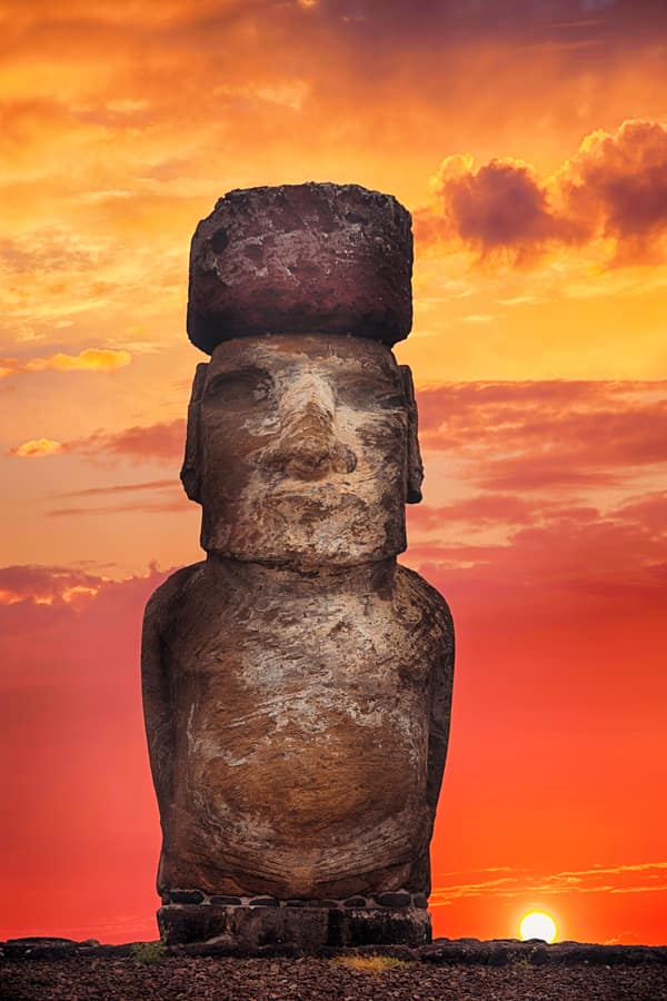 A moai and its topknot silhouetted against a fiery sunset