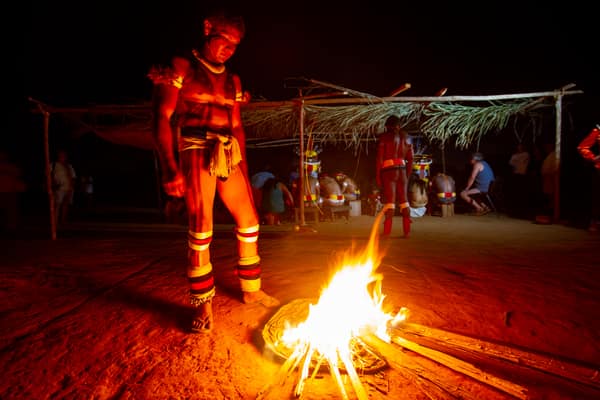 A dancer in body paint beside a ceremonial fire at night