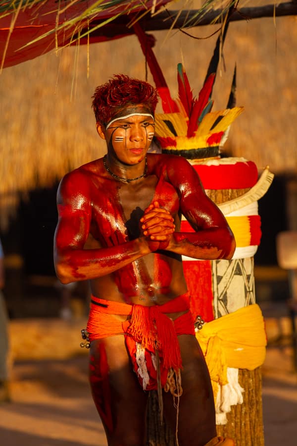 A young man in body paint beside a decorated ceremonial post