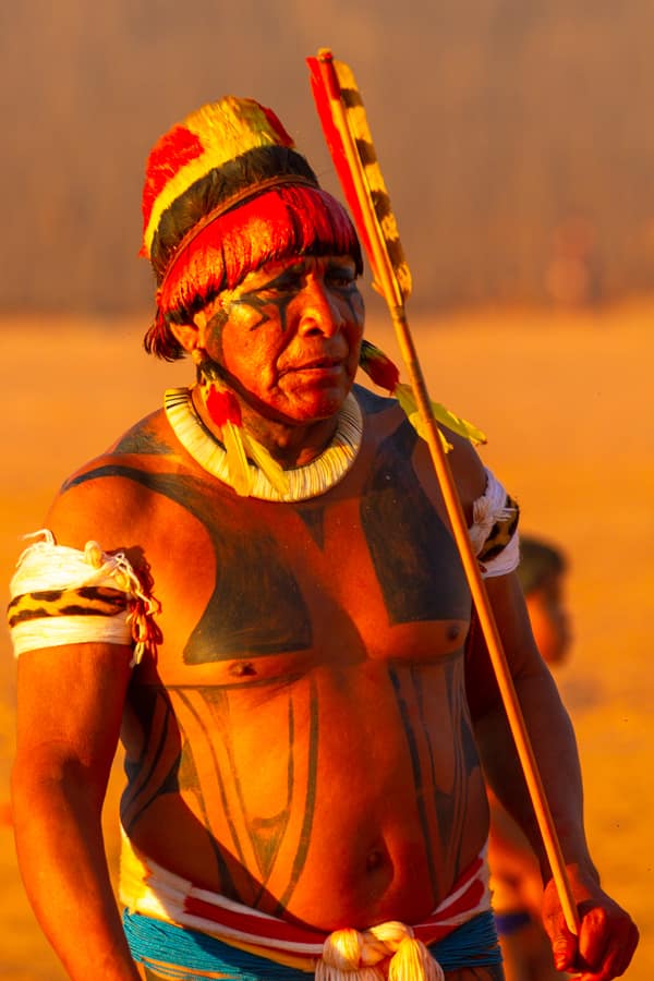 An elder in a feather headdress holding a ceremonial staff at sunset