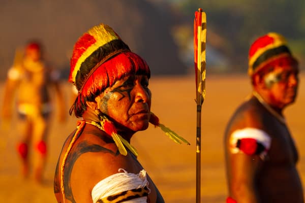 Men in feather headdresses and body paint gathered at sunset