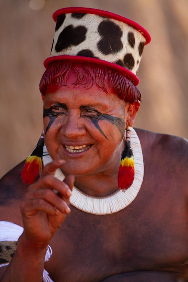 An elder woman wearing a feathered headdress and a shell necklace