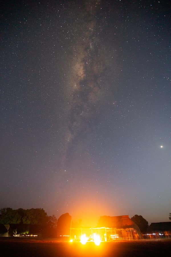 The Milky Way over the village at night above a glowing fire